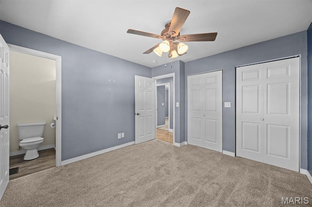 unfurnished bedroom with multiple closets, carpet floors, baseboards, ensuite bath, and a ceiling fan