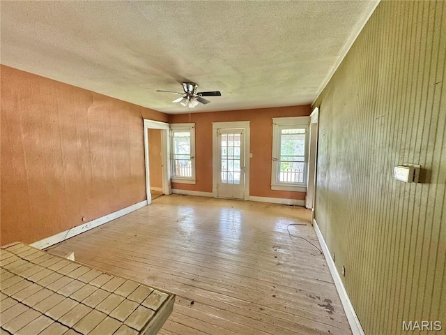 empty room featuring light wood finished floors, a textured ceiling, ceiling fan, wood walls, and baseboards