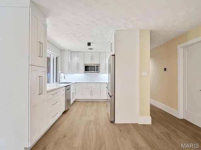 kitchen featuring appliances with stainless steel finishes, a sink, light wood-type flooring, white cabinets, and a textured ceiling