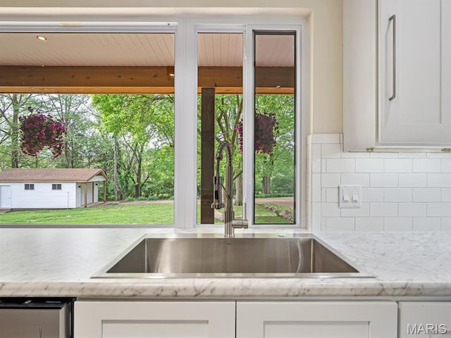 kitchen featuring a sink, decorative backsplash, white cabinets, and light stone countertops