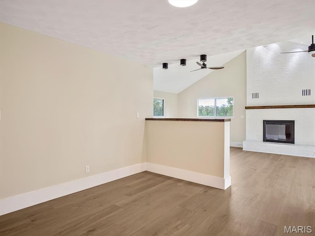 unfurnished living room with wood finished floors, baseboards, a textured ceiling, vaulted ceiling, and a ceiling fan