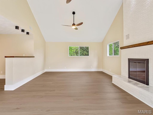 unfurnished living room with a ceiling fan, baseboards, wood finished floors, a brick fireplace, and high vaulted ceiling