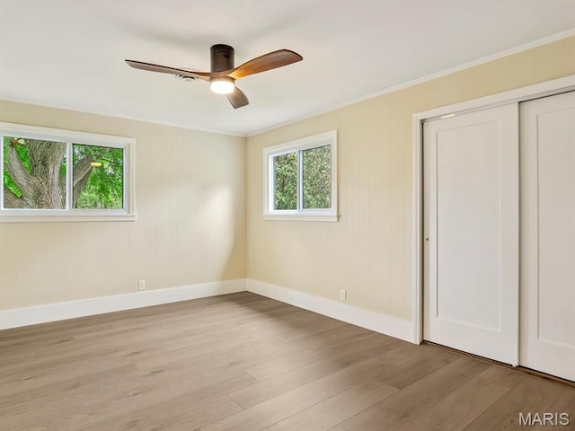 unfurnished bedroom featuring multiple windows, baseboards, light wood-type flooring, ornamental molding, and a closet