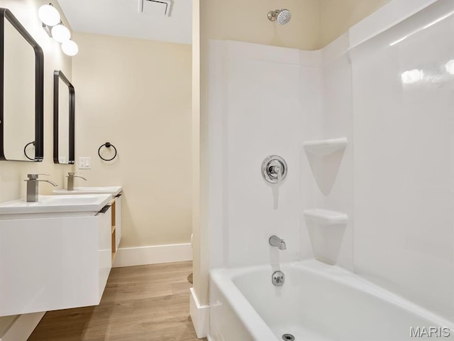 bathroom featuring wood finished floors, washtub / shower combination, double vanity, and baseboards