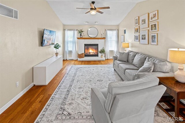 living area featuring lofted ceiling, ceiling fan, wood finished floors, baseboards, and a glass covered fireplace