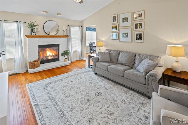 living area featuring vaulted ceiling, a brick fireplace, wood finished floors, and baseboards