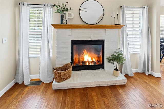 detailed view of a brick fireplace, baseboards, and wood finished floors