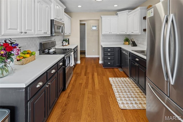 kitchen with appliances with stainless steel finishes, white cabinetry, baseboards, light wood-type flooring, and decorative backsplash