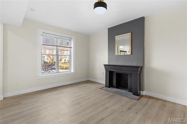 unfurnished living room featuring wood finished floors, baseboards, and a fireplace with flush hearth