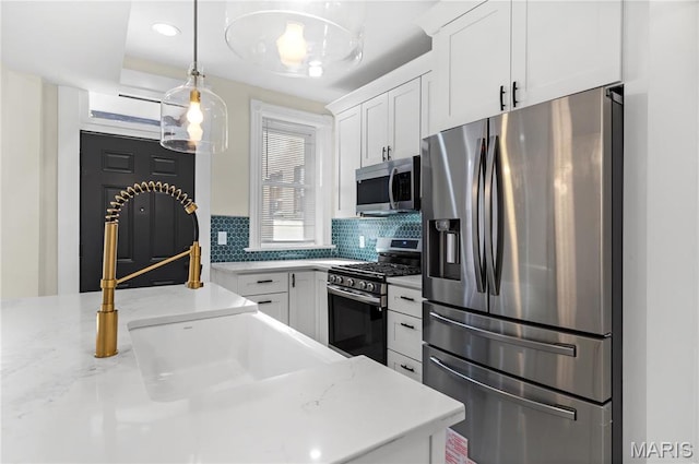 kitchen featuring appliances with stainless steel finishes, decorative backsplash, white cabinetry, hanging light fixtures, and a sink