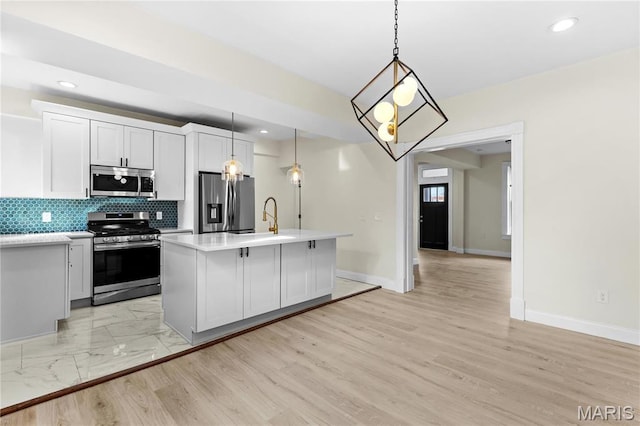 kitchen featuring appliances with stainless steel finishes, light countertops, baseboards, a sink, and an island with sink