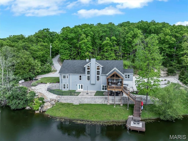 back of property with stairway, a lawn, a deck with water view, a forest view, and a chimney