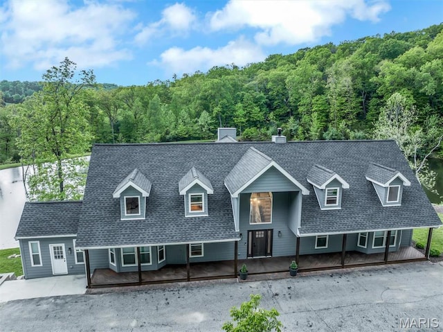 view of front of home featuring a forest view, a shingled roof, and covered porch