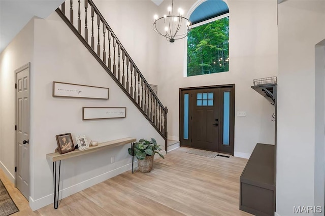 entryway featuring a chandelier, baseboards, a towering ceiling, stairs, and wood finished floors