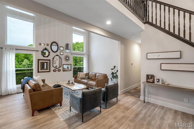 living room featuring a towering ceiling, light wood finished floors, baseboards, and recessed lighting