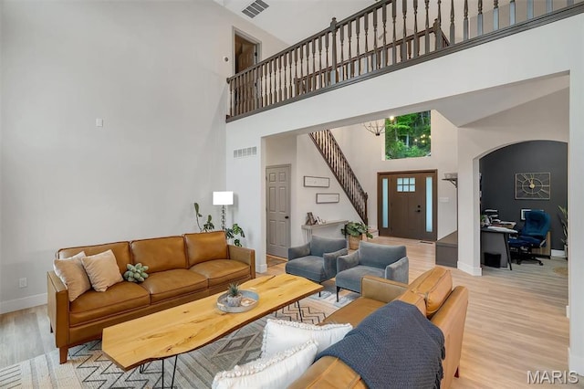 living room featuring a high ceiling, baseboards, light wood-style floors, stairway, and a desk
