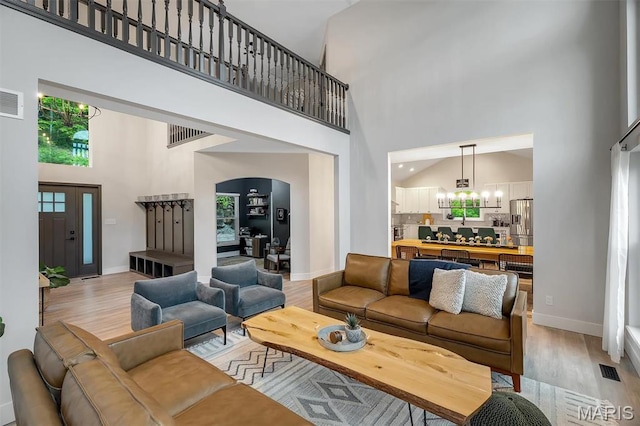 living area with a towering ceiling, light wood-style flooring, a chandelier, and baseboards