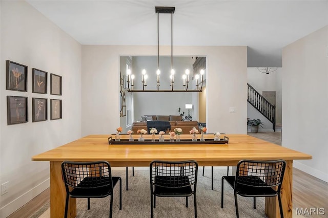 dining room with light wood-style floors, baseboards, a chandelier, and stairs