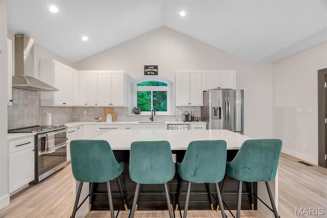 kitchen featuring stainless steel appliances, wall chimney exhaust hood, a breakfast bar, a sink, and vaulted ceiling