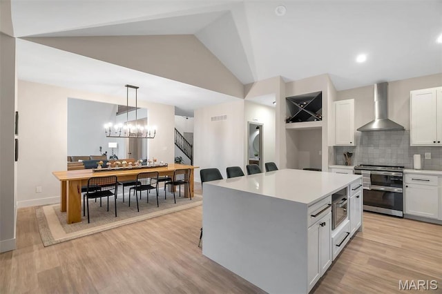 kitchen featuring stainless steel appliances, wall chimney exhaust hood, white cabinets, light countertops, and backsplash
