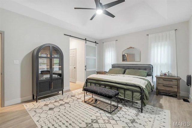 bedroom with a barn door, light wood-style flooring, baseboards, and ceiling fan