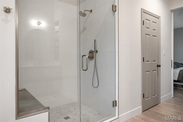 ensuite bathroom with a stall shower, wood finished floors, and baseboards