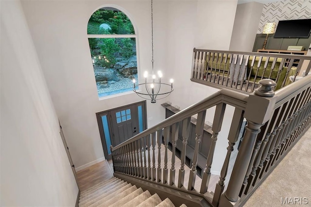 staircase featuring a chandelier, a towering ceiling, and baseboards