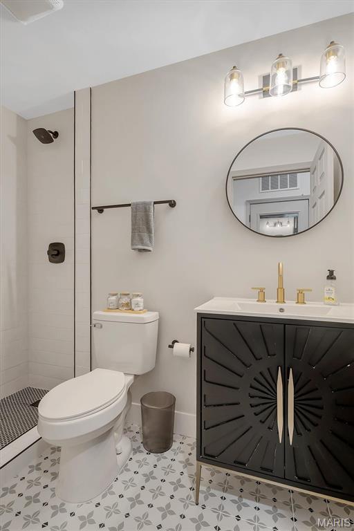 full bathroom featuring toilet, a tile shower, vanity, and baseboards