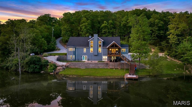 rear view of house with a wooded view, stairs, a yard, and a deck with water view