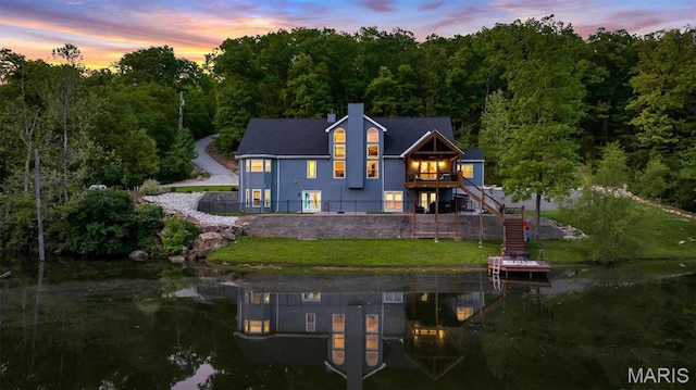 back of house featuring stairway, a water view, a forest view, a yard, and a chimney