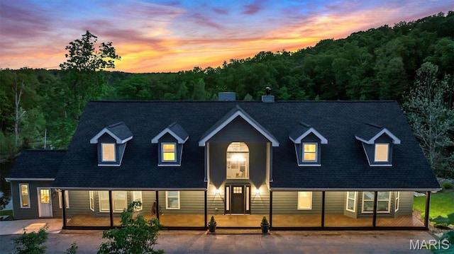 view of front of house with a porch, roof with shingles, and a forest view