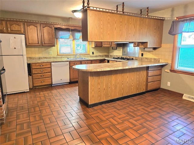 kitchen featuring white appliances, a peninsula, a sink, brick patterned flooring, and backsplash