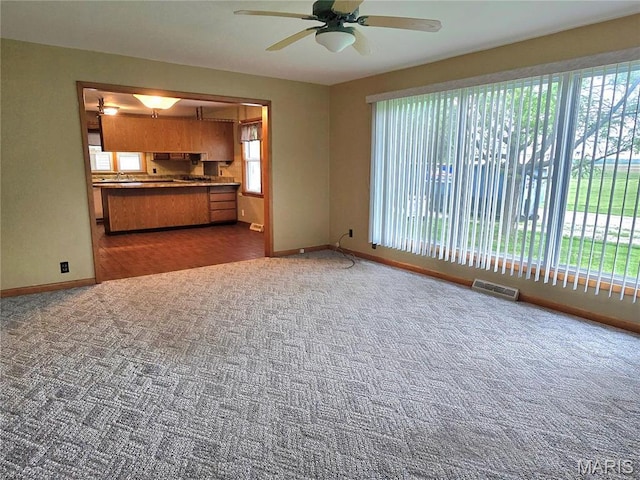 unfurnished living room featuring carpet flooring, baseboards, and ceiling fan