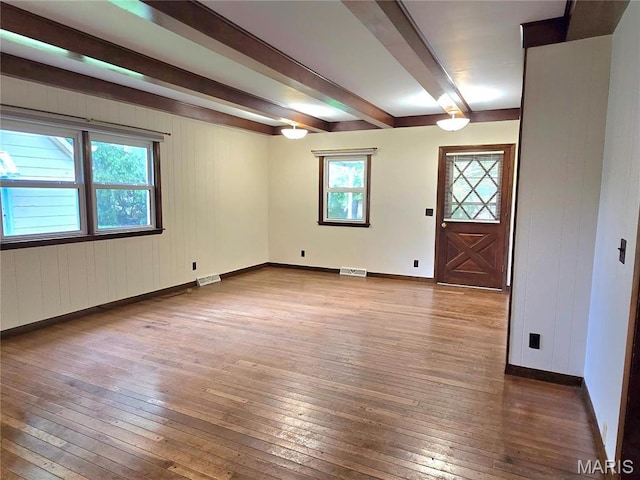 empty room with beam ceiling, wood-type flooring, baseboards, and wooden walls