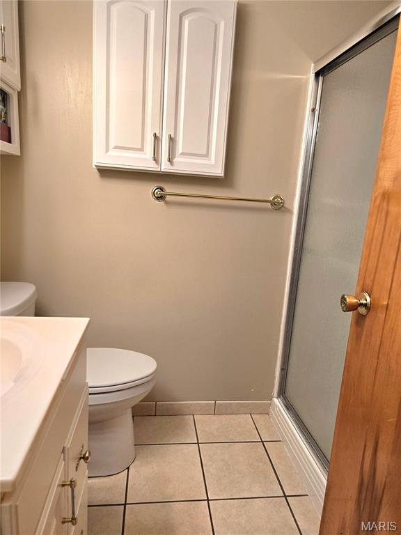 bathroom with toilet, tile patterned flooring, vanity, a stall shower, and baseboards