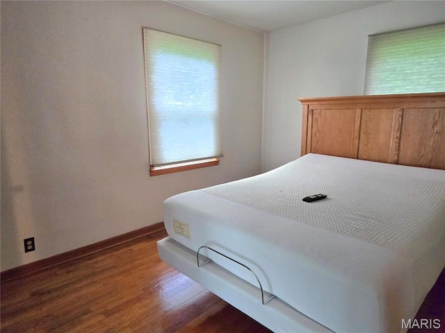bedroom with multiple windows, wood finished floors, and baseboards