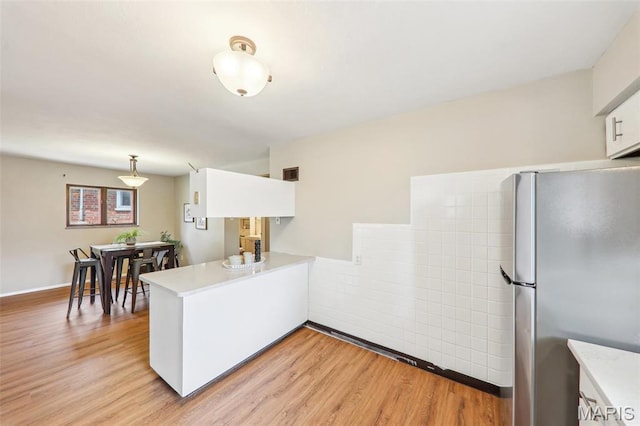 4116 Parker Ave, Saint Louis, MO 63116 - kitchen featuring freestanding refrigerator, a peninsula, light countertops, light wood-style flooring, and white cabinetry