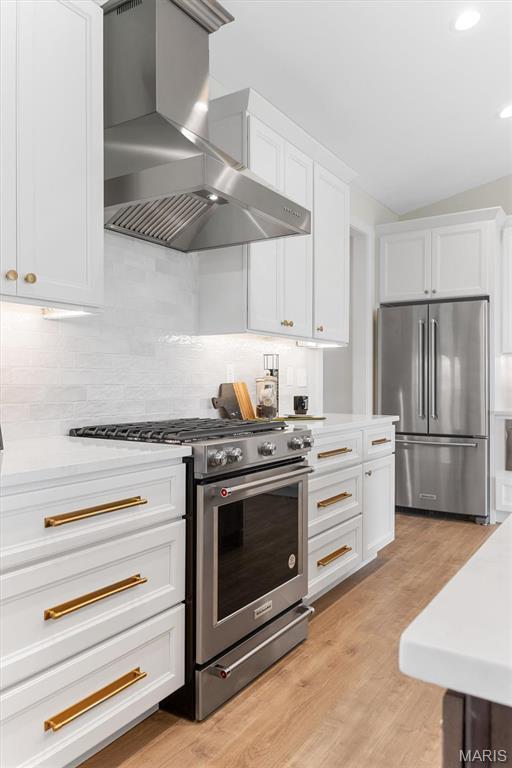 2217 Valleyview Dr, Barnhart, MO 63012 - kitchen featuring appliances with stainless steel finishes, wall chimney range hood, light countertops, white cabinetry, and vaulted ceiling