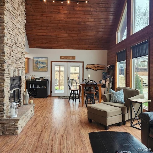 living area featuring high vaulted ceiling, healthy amount of natural light, track lighting, wood ceiling, and a stone fireplace