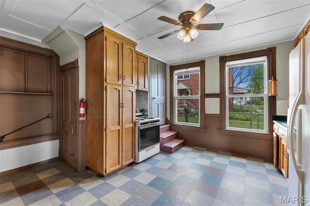 63 N Hanover St, Cape Girardeau, MO 63701 - kitchen with white range with gas stovetop, light flooring, ceiling fan, brown cabinetry, and a wainscoted wall