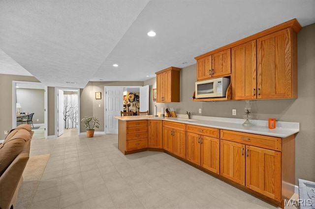 1674 Lakepointe Estates Dr, Ofallon, IL 62269 - kitchen with white microwave, a peninsula, light countertops, brown cabinets, and recessed lighting