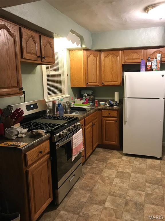 340 Kemper St, Troy, MO 63379 - kitchen with freestanding refrigerator, gas range, dark countertops, a sink, and brown cabinetry