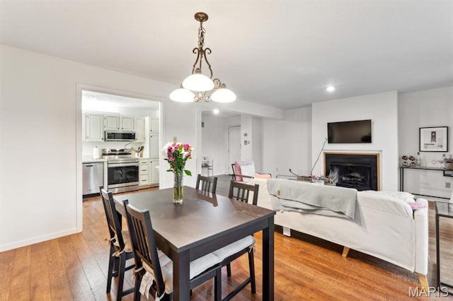 dining space featuring a fireplace, light wood finished floors, and baseboards