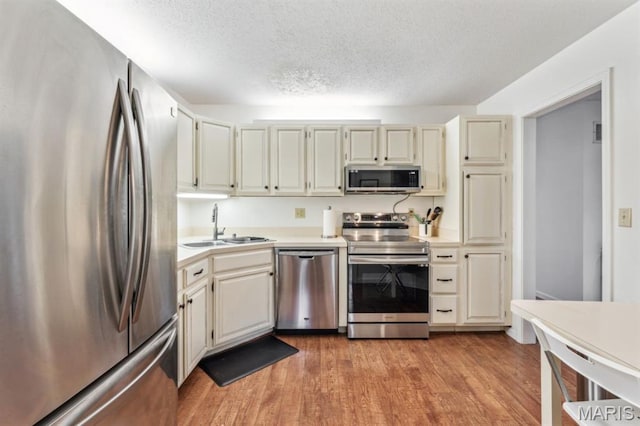 kitchen featuring stainless steel appliances, a sink, light countertops, light wood-style floors, and a textured ceiling