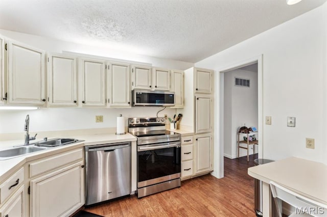 kitchen featuring stainless steel appliances, a sink, a textured ceiling, light countertops, and light wood finished floors