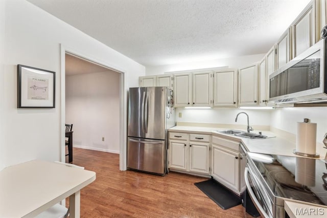 kitchen featuring stainless steel appliances, a sink, a textured ceiling, light wood-style flooring, and light countertops