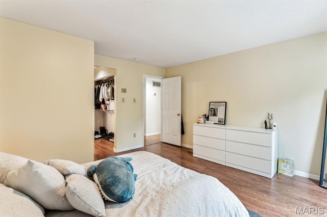 bedroom with wood finished floors, baseboards, a walk in closet, and a closet
