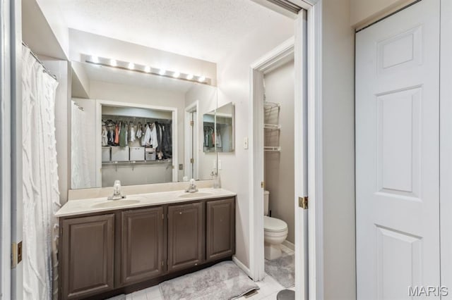 bathroom featuring toilet, double vanity, a spacious closet, and a textured ceiling