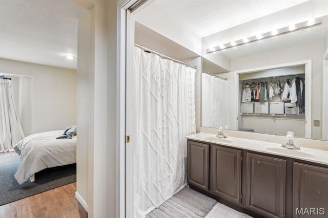 ensuite bathroom with double vanity, a textured ceiling, a closet, and wood finished floors