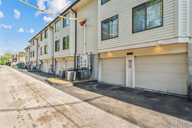 view of property exterior with a garage, asphalt driveway, a residential view, and cooling unit